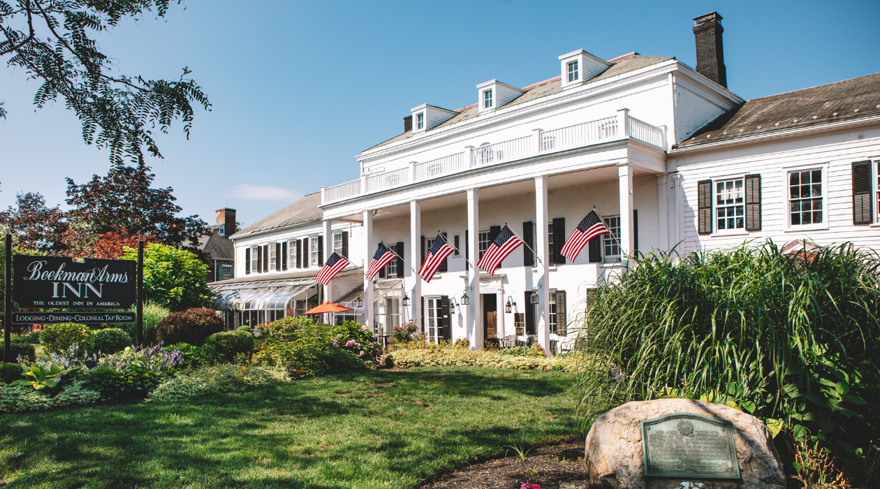 white exterior of 18th century building the beekman arms and delamater inn in rhinebeck american flags are set up on the green lawn